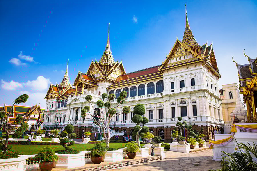 Grand Palace in Bangkok : "The Grand Palace in Bangkok, Thailand, showcasing traditional Thai architecture with ornate spires, white facades, and landscaped gardens under a clear blue sky"