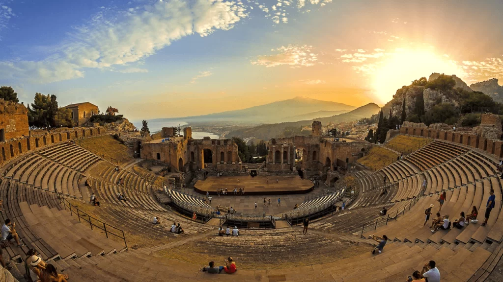 Ephesus ancient Roman city: "Ancient Roman amphitheater at sunset with scenic mountain and sea views, historic ruins, and visitors exploring the site under golden light"