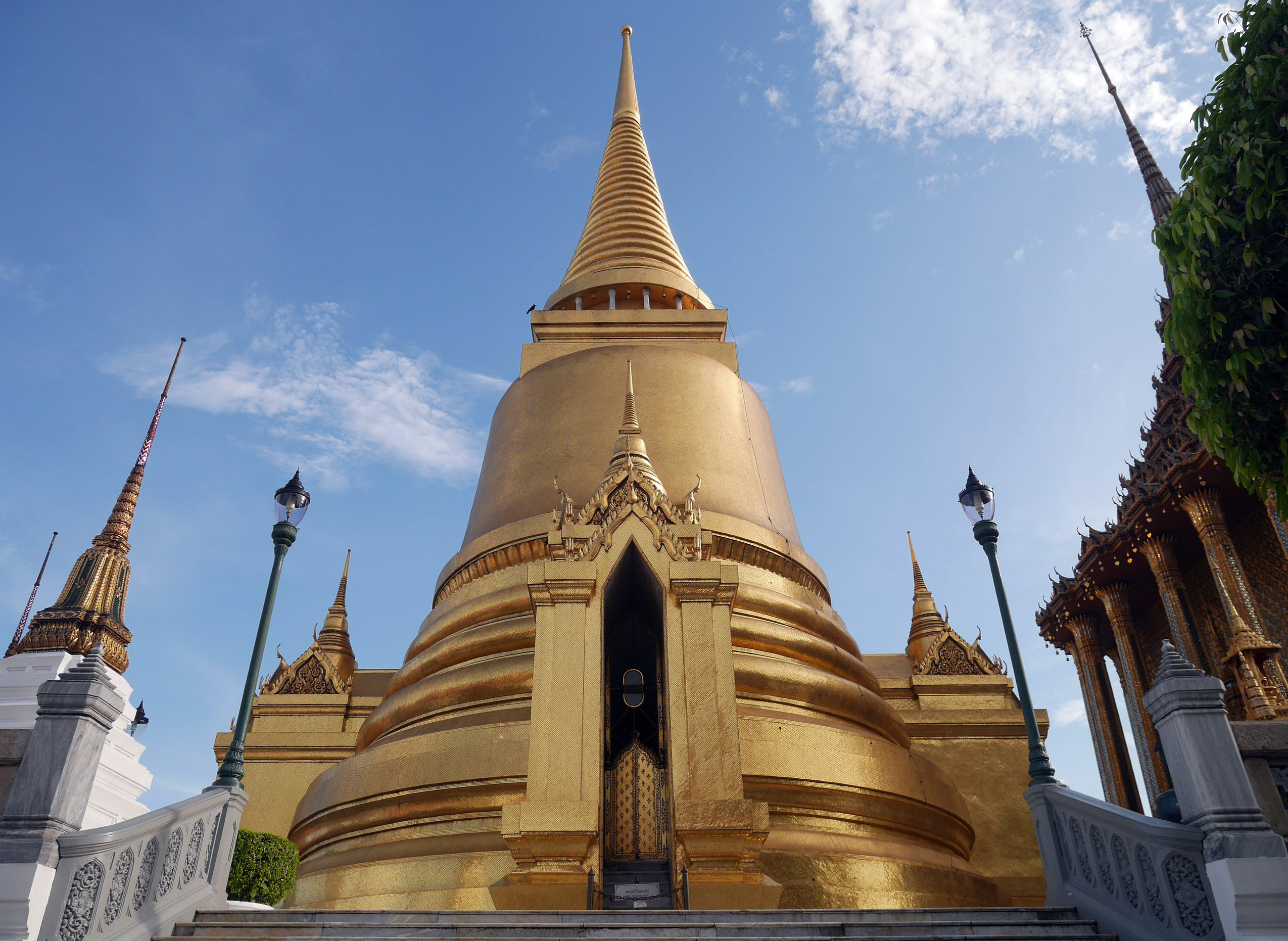 "Golden stupa at Wat Phra Kaew within the Grand Palace complex in Bangkok, Thailand, shining under a clear blue sky with intricate Thai architecture"