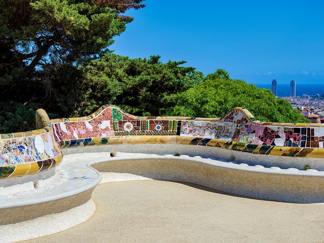 "Colorful mosaic serpentine bench at Park Güell in Barcelona, Spain, with panoramic city and sea views in the background on a sunny day"