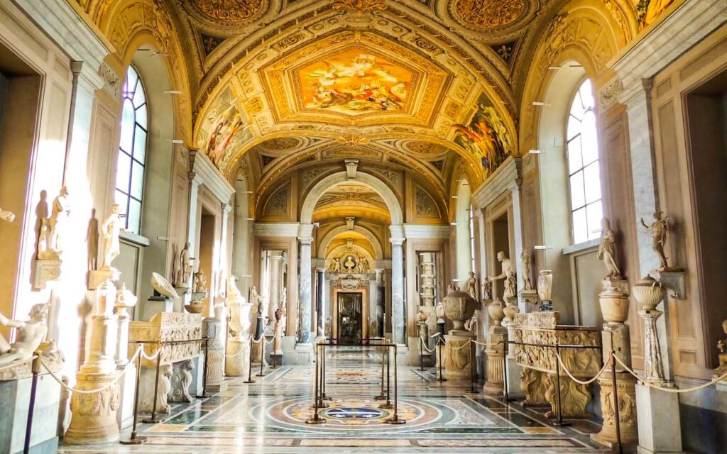 Vatican City travel guide: "Golden-ceiling hallway of the Vatican Museums in Vatican City adorned with classical sculptures, marble floors, and Renaissance artwork"