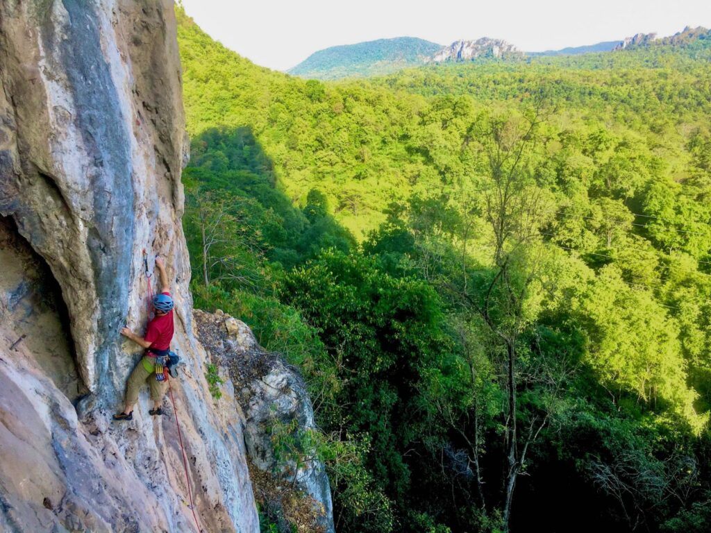 Thailand Phi Phi Islands "A rock climber scaling a limestone cliff in Thailand with lush green forest and distant mountains in the background"
