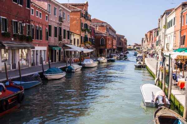 "Scenic canal view in Venice, Italy, with colorful historic buildings, small boats, and waterfront cafés on a sunny day"