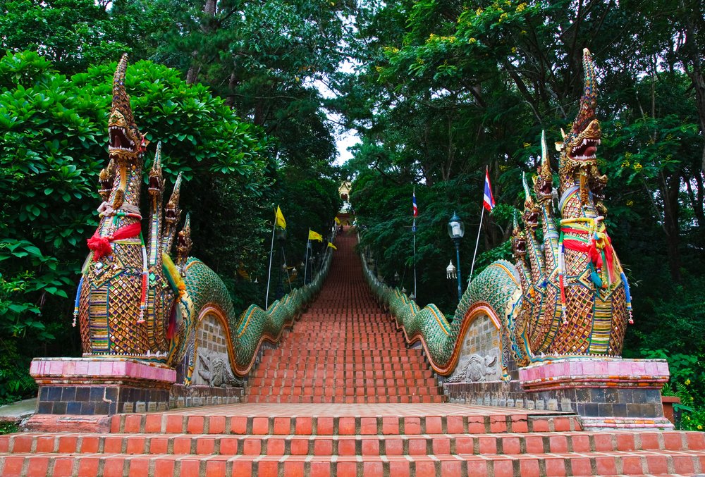 "Ornate Naga serpent staircase leading to Wat Phra That Doi Suthep temple in Chiang Mai, Thailand, surrounded by lush green forest"