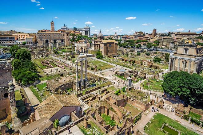 "Aerial view of the Roman Forum in Rome, Italy, showing ancient ruins, temples, and historic architecture under a bright blue sky"
