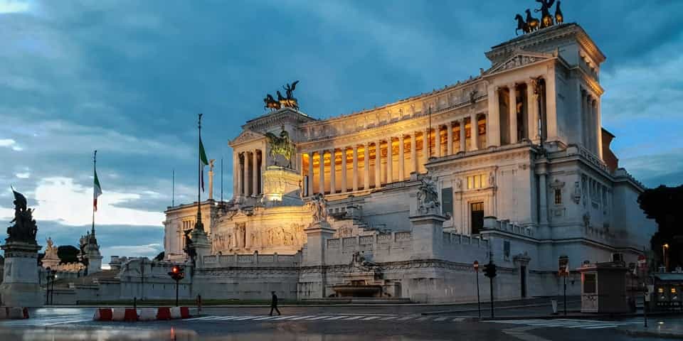 The Colosseum Rome travel guide: "The Altare della Patria monument in Rome, Italy, beautifully illuminated at dusk with dramatic clouds in the sky"
