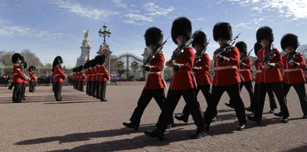 "Changing of the Guard ceremony at Buckingham Palace in London with soldiers in red uniforms and bearskin hats marching in formation"