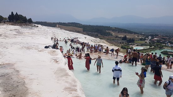 Pamukkale Thermal Pools: "Tourists walking barefoot through the natural travertine thermal pools of Pamukkale, Turkey, surrounded by white calcium terraces and scenic mountain views"
