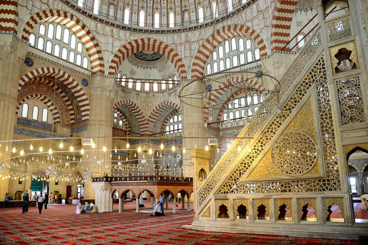 Blue Mosque Istanbul: “Interior of the Selimiye Mosque in Edirne, Turkey, showcasing its grand dome, red-and-white arches, ornate calligraphy, and illuminated chandeliers above the patterned prayer carpet.”