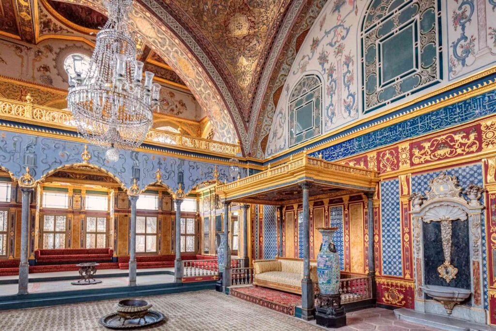 "Lavishly decorated room inside Topkapi Palace in Istanbul, Turkey, featuring intricate Ottoman architecture, chandeliers, colorful tiles, and golden details"