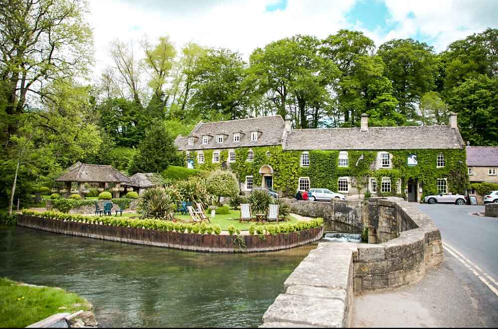 Lake District National Park: "Charming riverside cottage and inn covered in green ivy in a peaceful English countryside village surrounded by lush trees and a stone bridge"