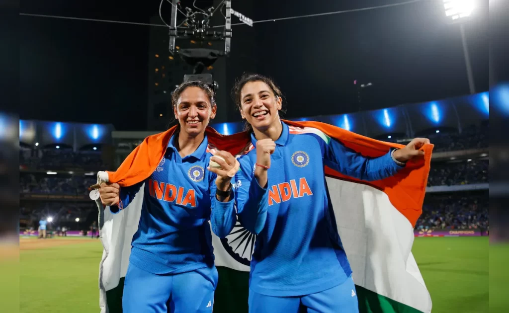 Indian women’s cricket players celebrating World Cup victory with the national flag draped around their shoulders at DY Patil Stadium.
