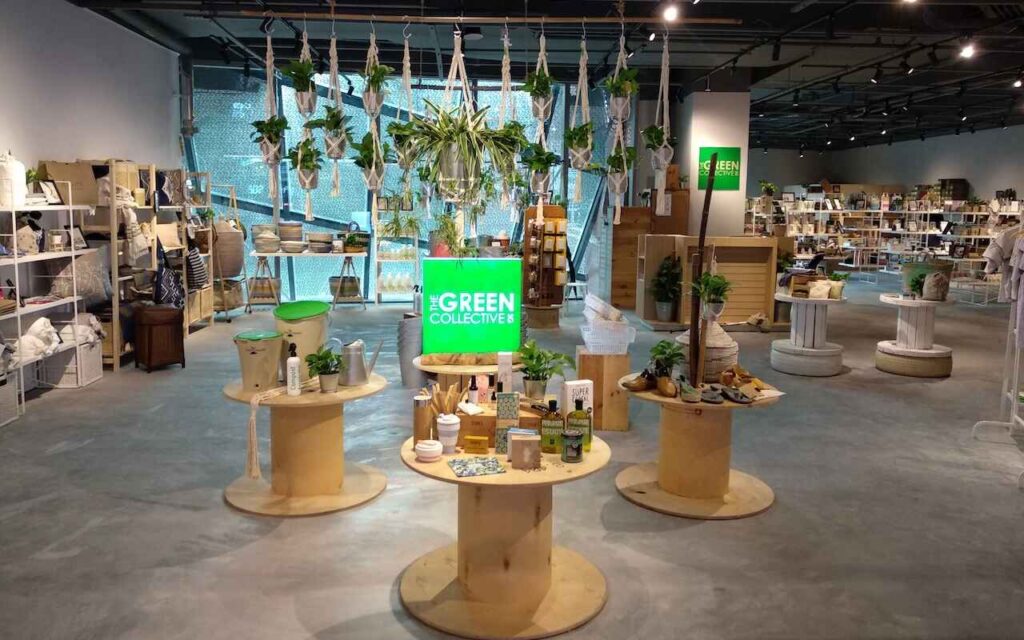 “Eco-friendly store interior displaying sustainable products, reusable items, indoor plants, and green living essentials arranged on wooden tables at The Green Collective.”