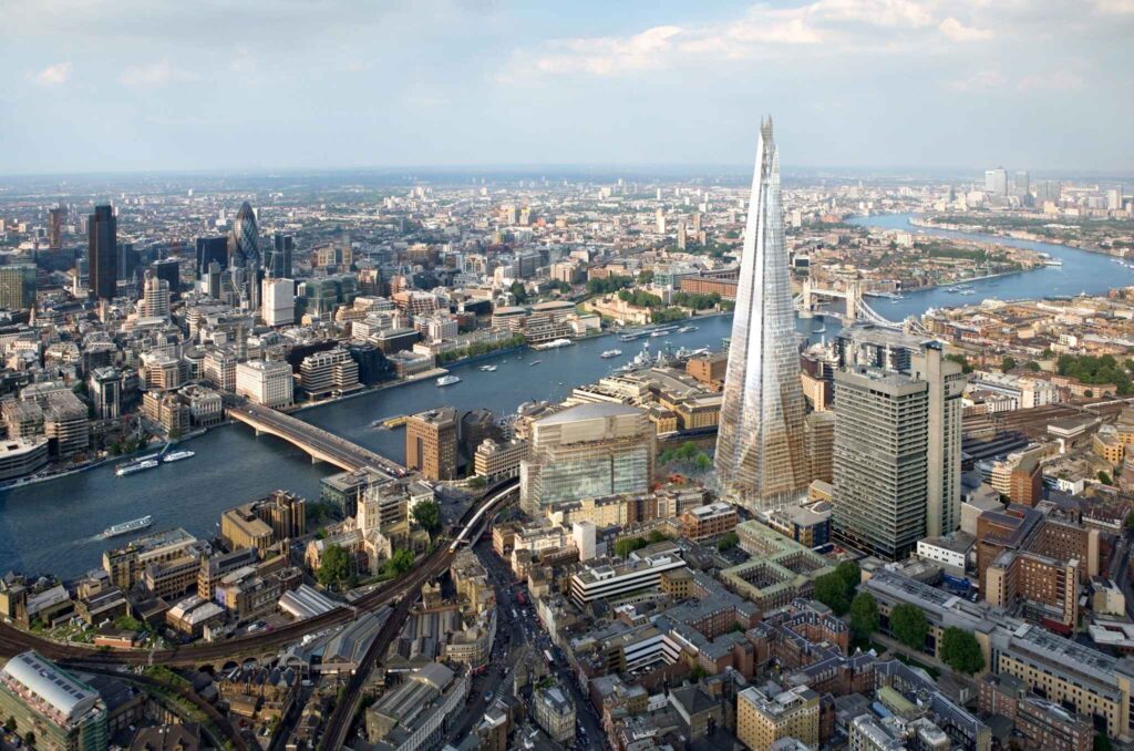 "Aerial view of London city skyline featuring the Shard skyscraper, Tower Bridge, and the River Thames on a clear day"