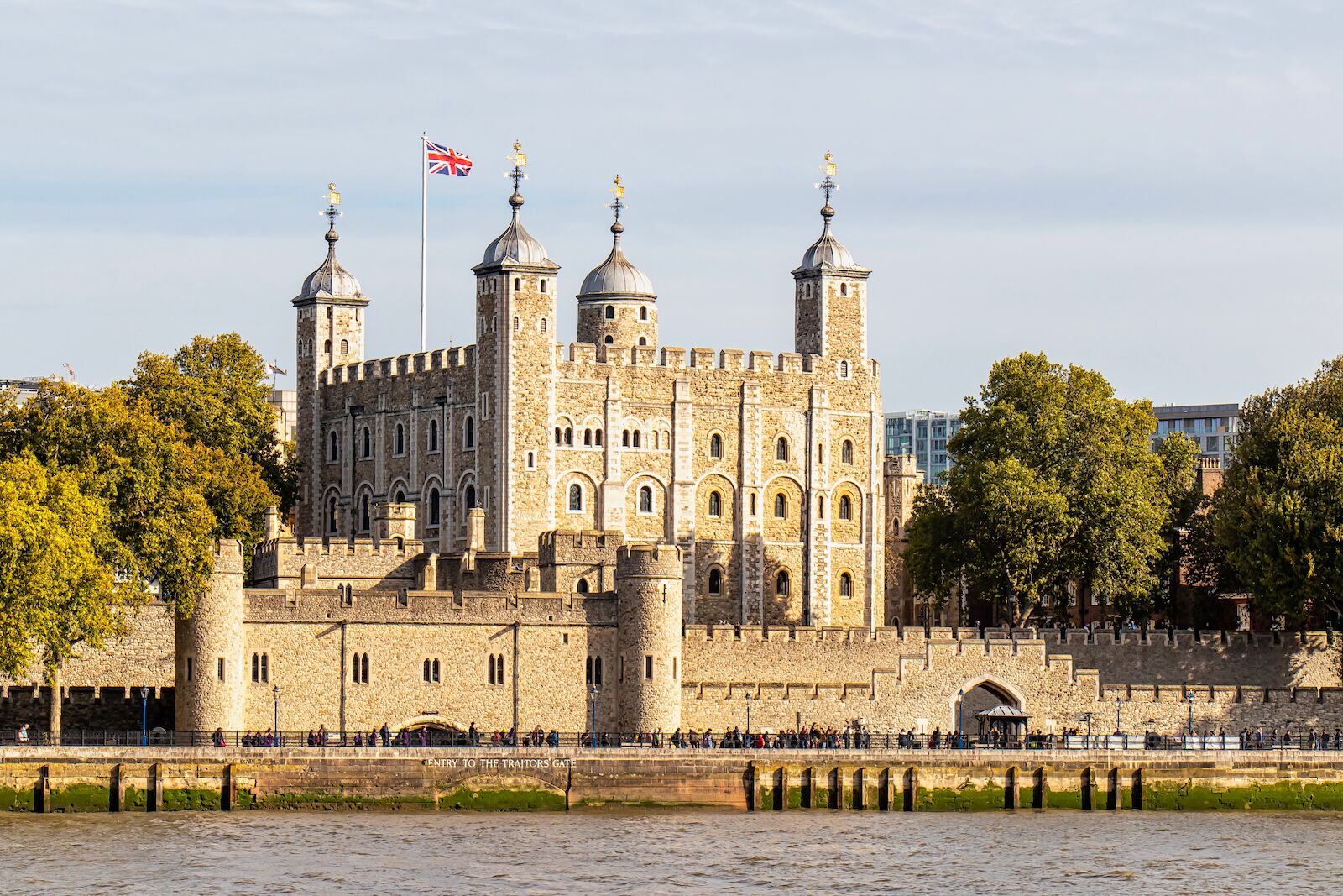 "The Tower of London historic fortress on the River Thames with the Union Jack flag flying above, surrounded by medieval walls and trees in central London, England"