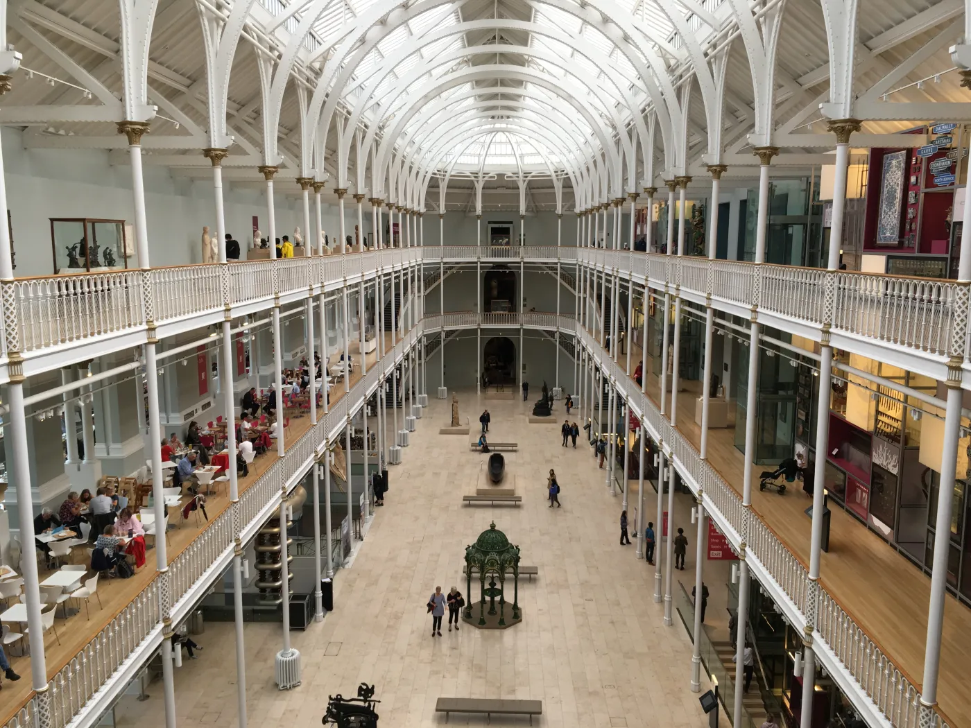 "Interior view of the National Museum of Scotland in Edinburgh featuring Victorian architecture, high glass ceilings, and visitors exploring the central gallery exhibits."
