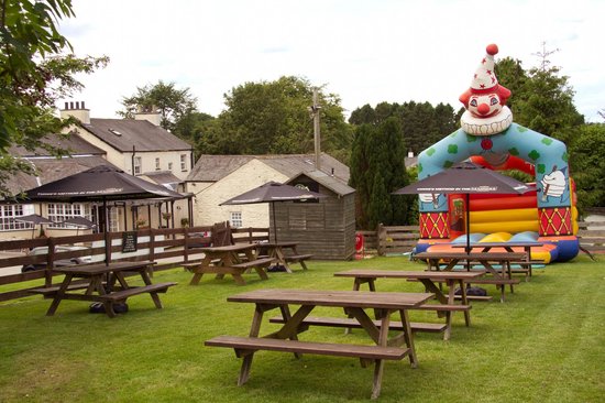 "Outdoor pub garden with wooden picnic tables and a colorful inflatable play area in a countryside village in England during summer"
